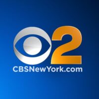 The image shows the logo for CBS New York (WCBS-TV Channel 2). It features the iconic silver CBS "Eye" logo next to a large, stylized orange number 2, set against a blue gradient background. Below the logo, the text CBSNewYork.com is written in white.