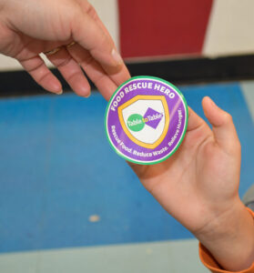 A Willard Elementary School student receives a Food Rescue Hero badge from Table to Table.