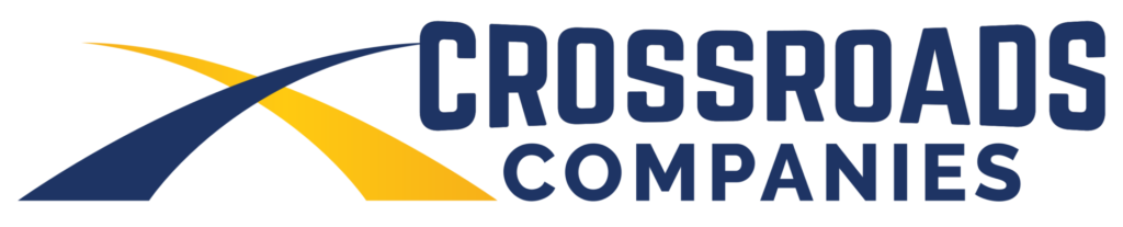Crossroads Companies logo featuring two intersecting, curved path graphic lines in dark blue and yellow on the left, followed by the text "CROSSROADS" stacked above "COMPANIES" in bold, dark blue capital letters.